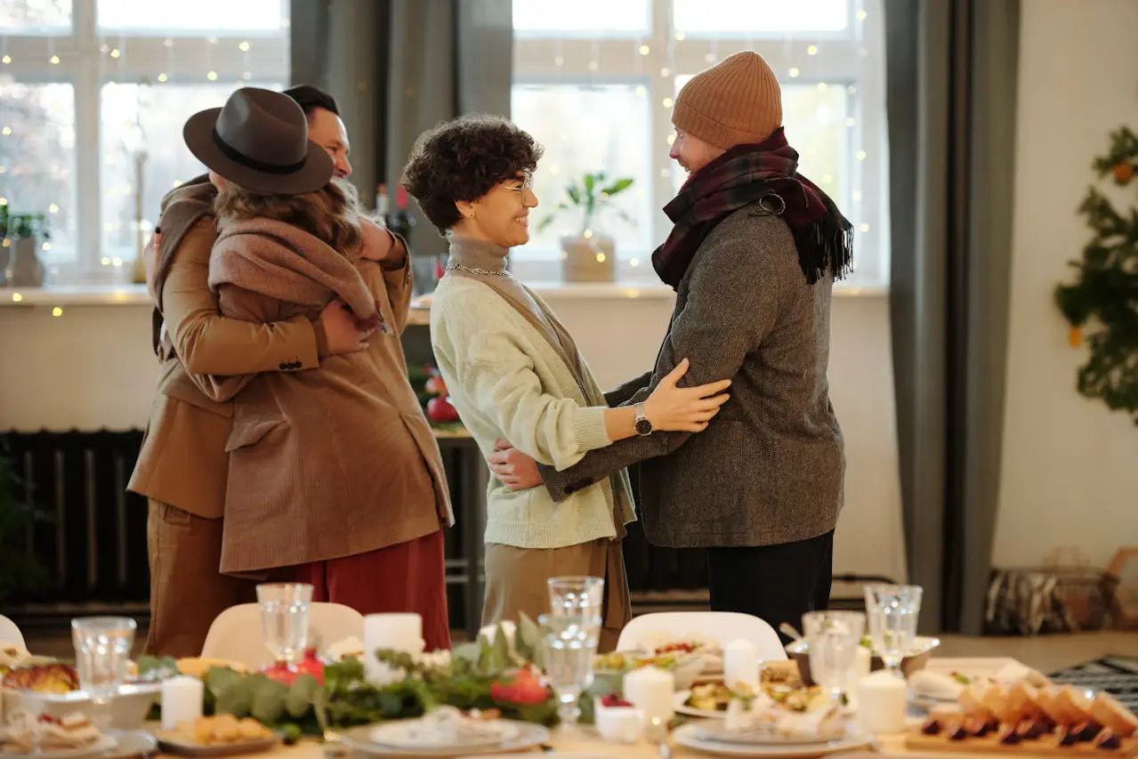 Three people embrace joyfully at a festive Christmas dinner table, surrounded by holiday decorations and food